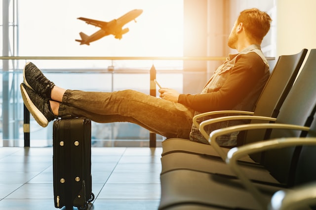 man sitting at airport looking at plane taking off